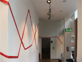 Interuptions (embroidered red ribbon installed on white walls in gallery